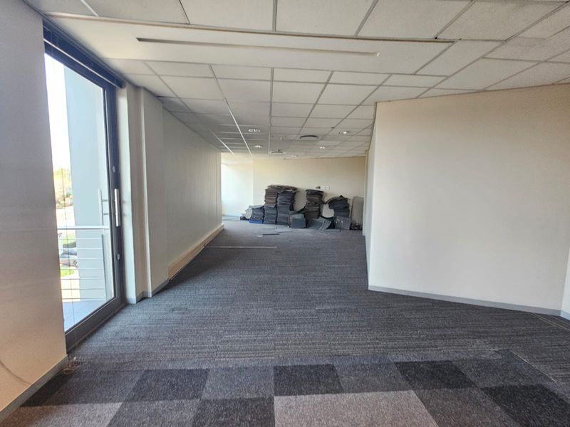 An empty office space featuring a suspended ceiling, carpet tile flooring, and a sliding glass door providing natural light.