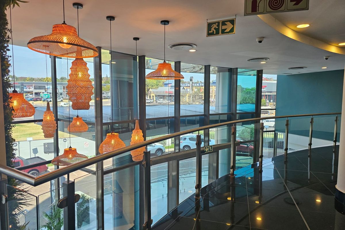 Modern office building hallway featuring floor-to-ceiling glass windows, a sleek glass balustrade, and polished tiled flooring with integrated safety signage.