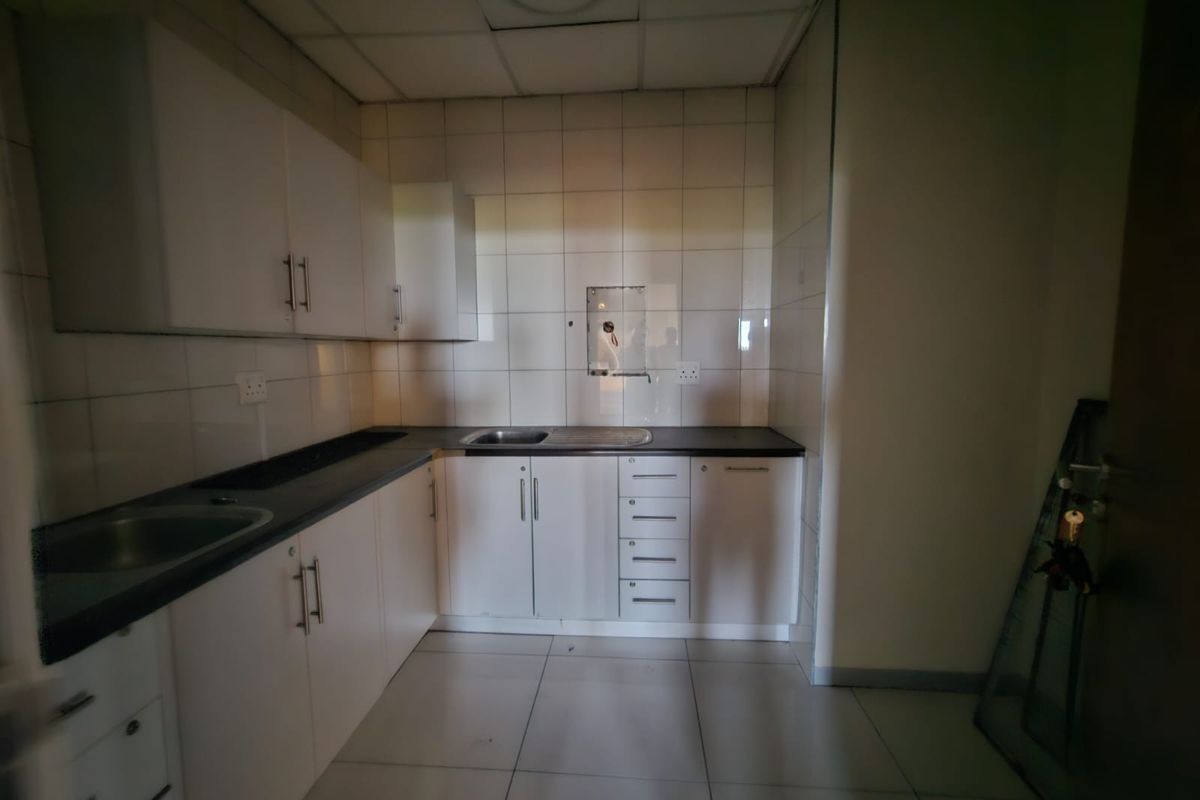 A functional office kitchenette featuring white built-in cabinetry, dark laminate countertops, a stainless steel sink, and tiled finishes throughout.