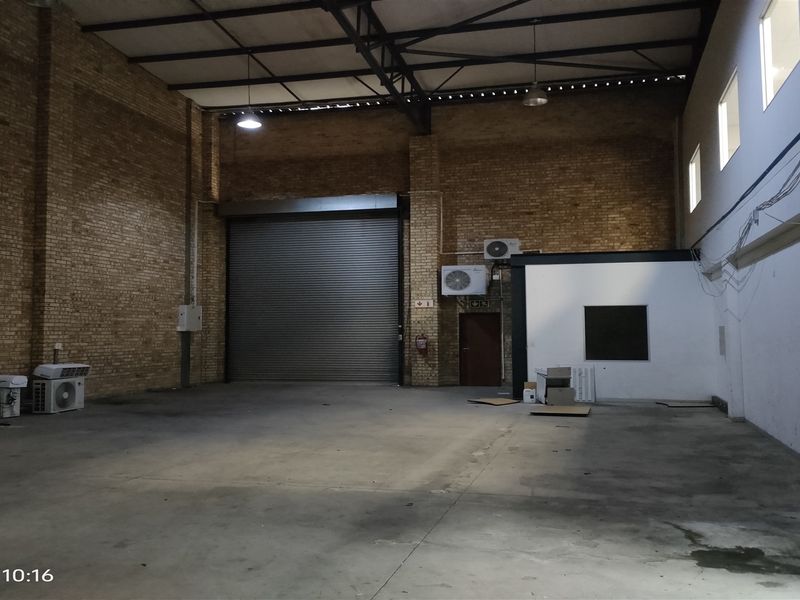 Spacious industrial warehouse unit featuring high ceilings, exposed brickwork, concrete flooring, and a large roller shutter door for easy access.