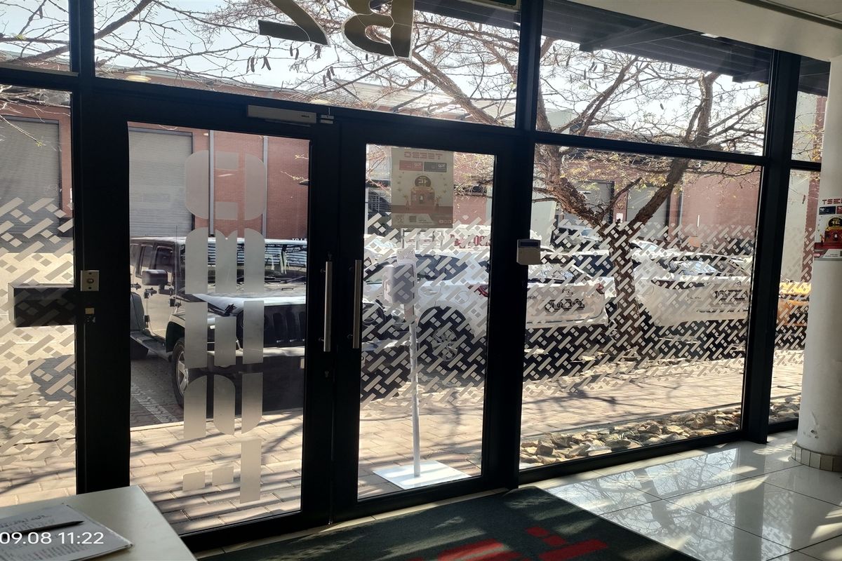 Modern industrial entrance area featuring large floor-to-ceiling glass panels and aluminium framed doors, providing clear views of the exterior parking area.