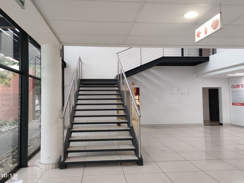 Spacious industrial entrance lobby featuring a modern metal staircase, large glass windows, and polished tiled flooring in a well-maintained commercial setting.