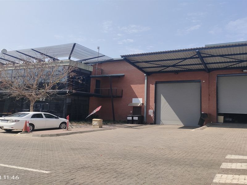 Front elevation of an industrial property featuring brick facade, large roller shutter doors, and a modern glass-fronted office section with a paved driveway.