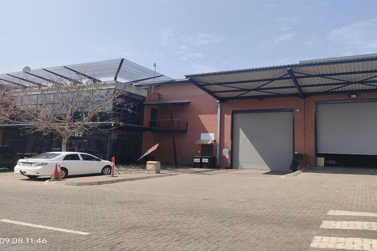 Front elevation of an industrial property featuring brick facade, large roller shutter doors, and a modern glass-fronted office section with a paved driveway.