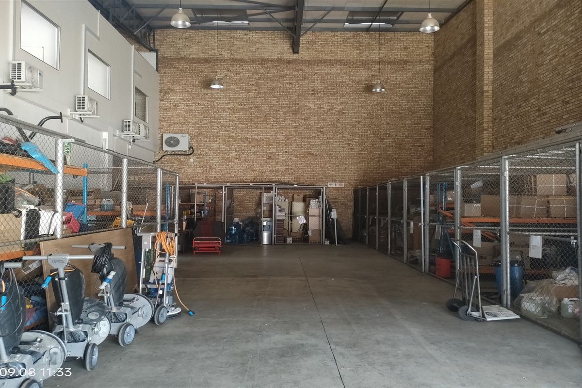 Industrial utility space featuring high ceilings with exposed steel trusses, brick walls, concrete flooring, and multiple chain-link storage partitions.