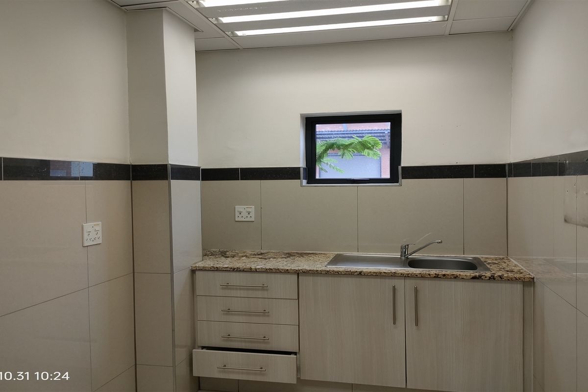 A functional kitchen area featuring granite countertops, stainless steel sink, built-in cabinetry, and tiled splashbacks in a clean, neutral finish.
