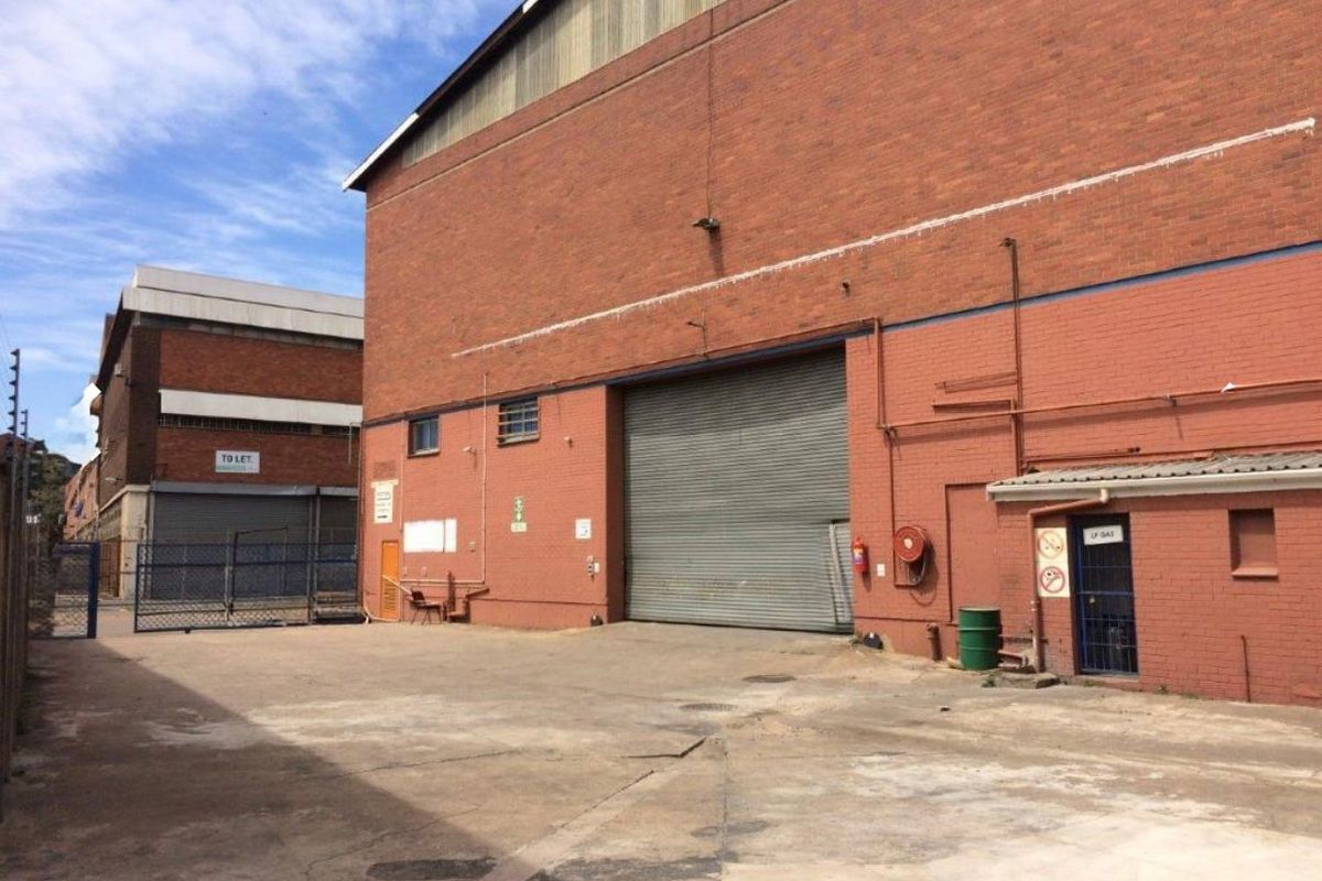 Industrial rear yard area featuring a large roller shutter door, brick facade, and secure access gate, suitable for logistics or storage operations.