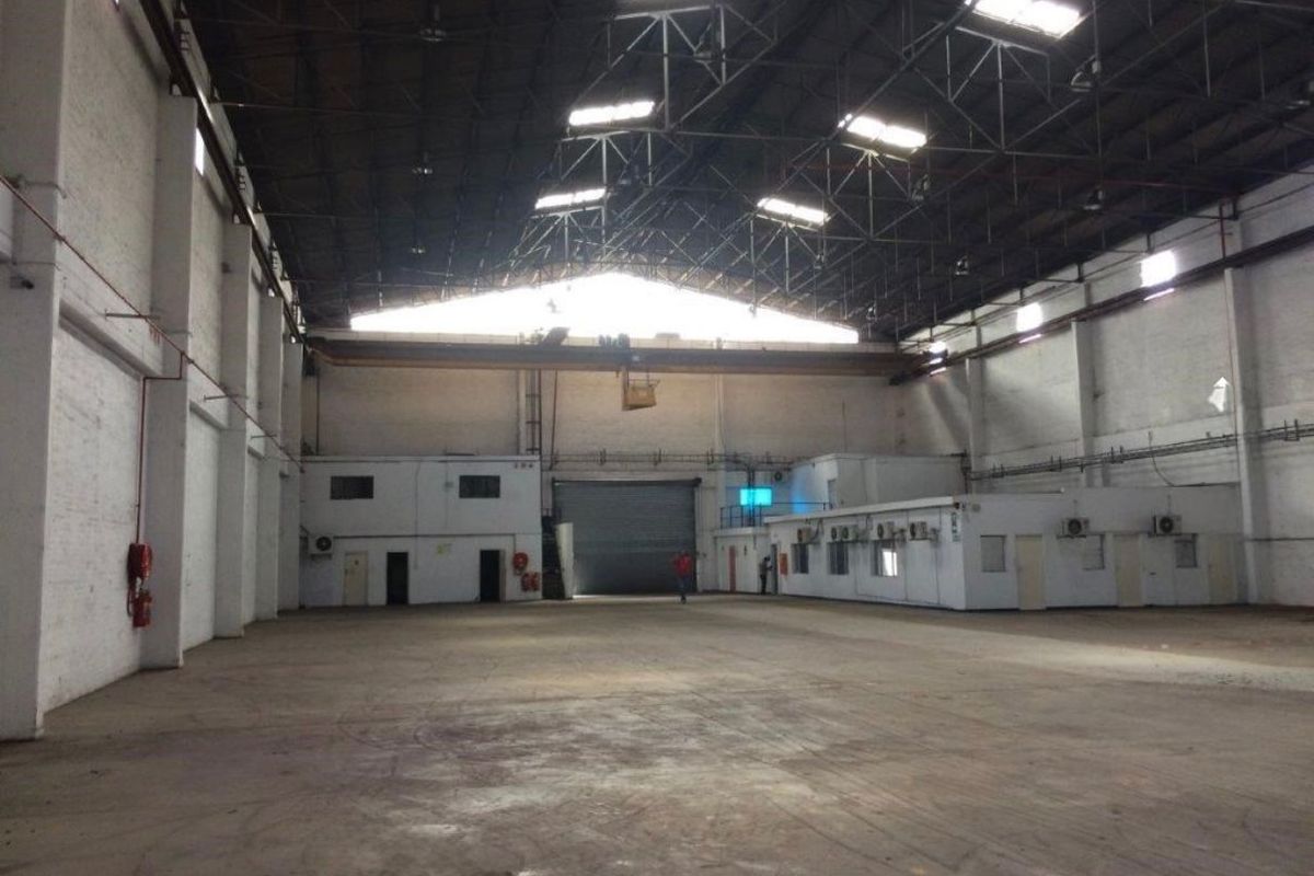 Spacious industrial warehouse featuring high ceilings with exposed steel trusses, overhead crane, concrete flooring, and integrated office or utility blocks.