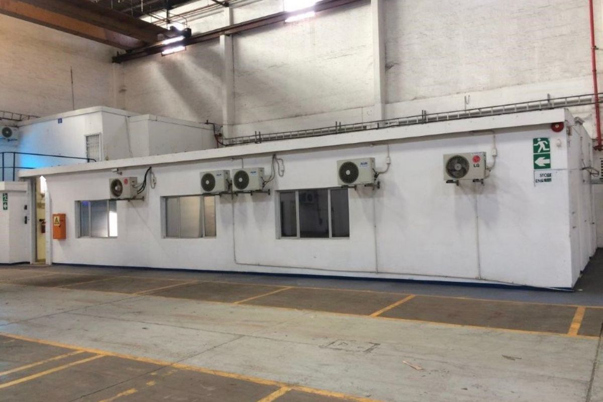A large industrial utility space featuring high ceilings with exposed steel trusses, concrete flooring, and multiple wall-mounted air conditioning units.