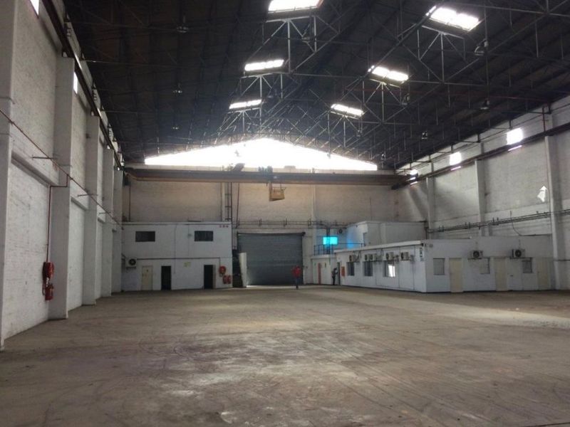 Spacious industrial warehouse featuring high ceilings with exposed steel trusses, overhead crane, concrete flooring, and integrated office or utility blocks.