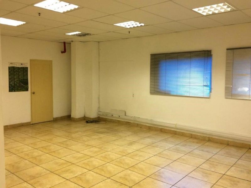 An empty industrial office space featuring tiled flooring, suspended ceiling with recessed lighting, and venetian blinds on the windows.