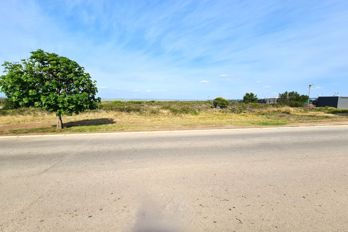 A street-level view of a vacant commercial land plot featuring paved road access, perimeter fencing, and open landscape.