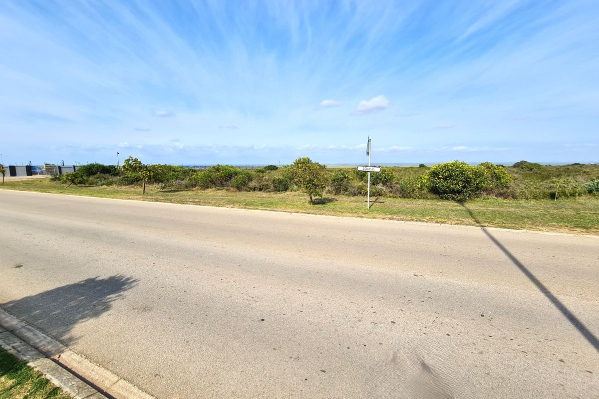 A view of the paved road and verge adjacent to the vacant commercial land, featuring clear street access and surrounding coastal vegetation.