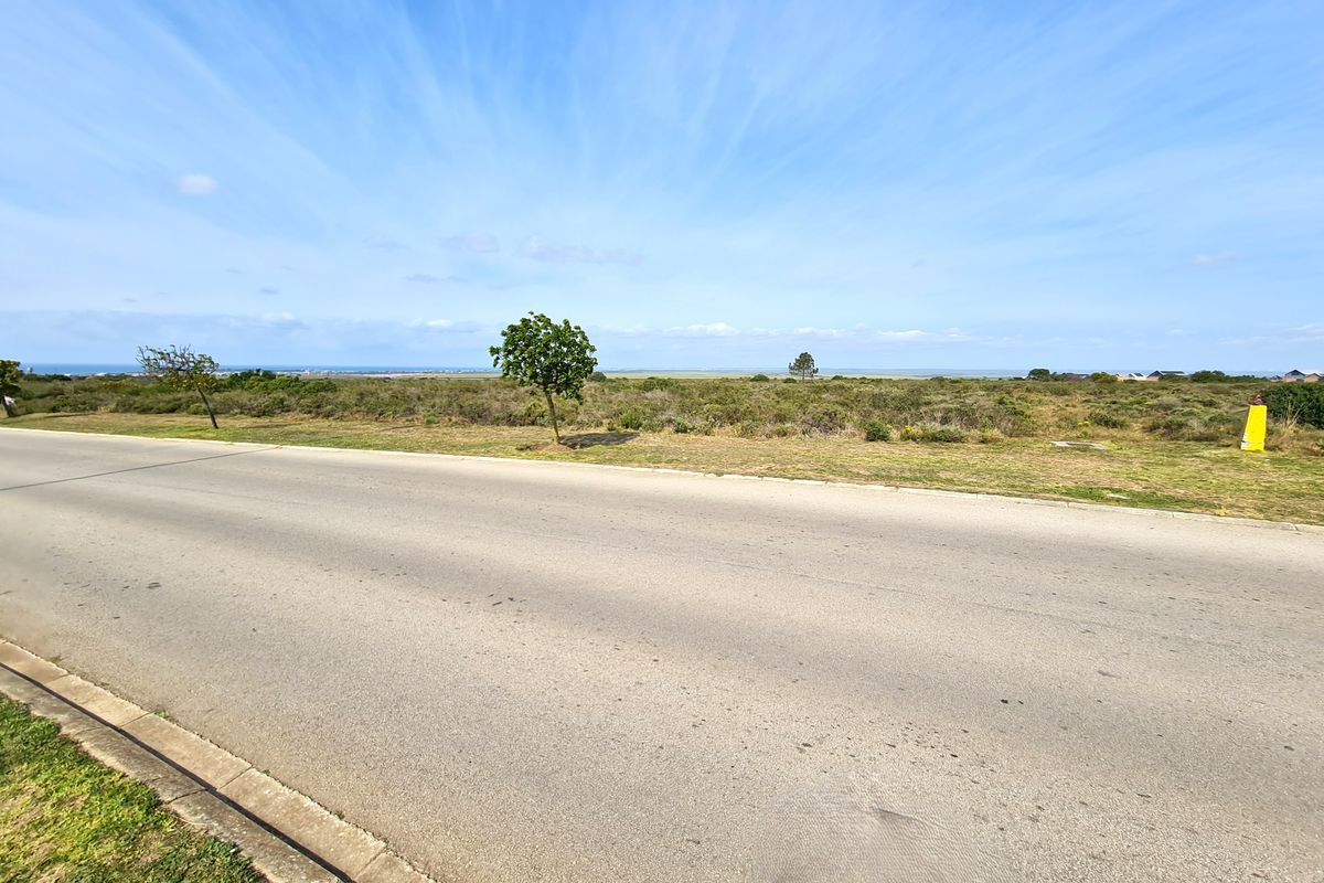 A street-level view of a vacant commercial land plot featuring an asphalt road and concrete curbing with natural landscape in the background.