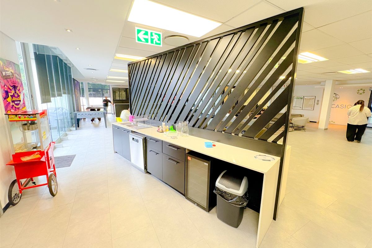 Modern office kitchenette featuring sleek cabinetry, integrated under-counter appliances, and a decorative black metal privacy screen in an open-plan workspace.