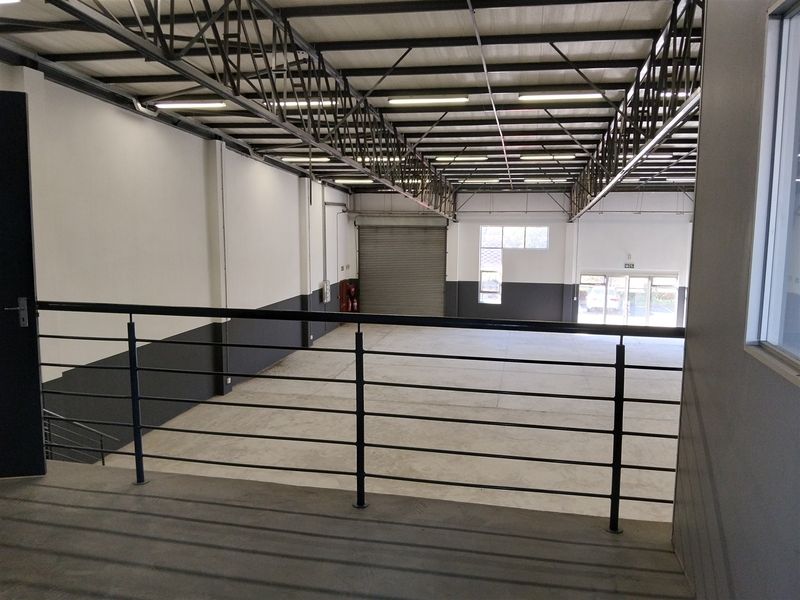 Spacious industrial warehouse interior featuring a mezzanine level, high-clearance steel truss ceiling, roller shutter door, and concrete flooring.