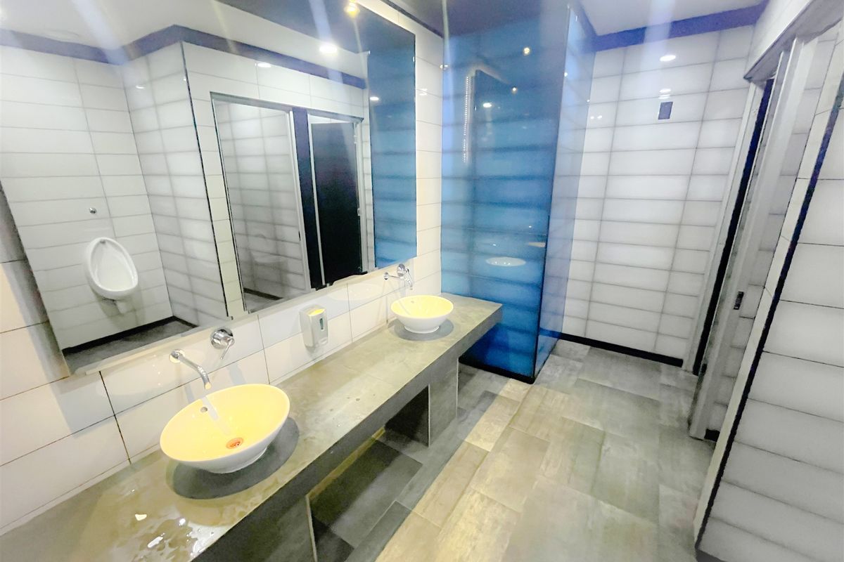 Modern office restroom featuring a concrete vanity with dual vessel sinks, large wall-mounted mirror, tiled walls, and a separate urinal area.