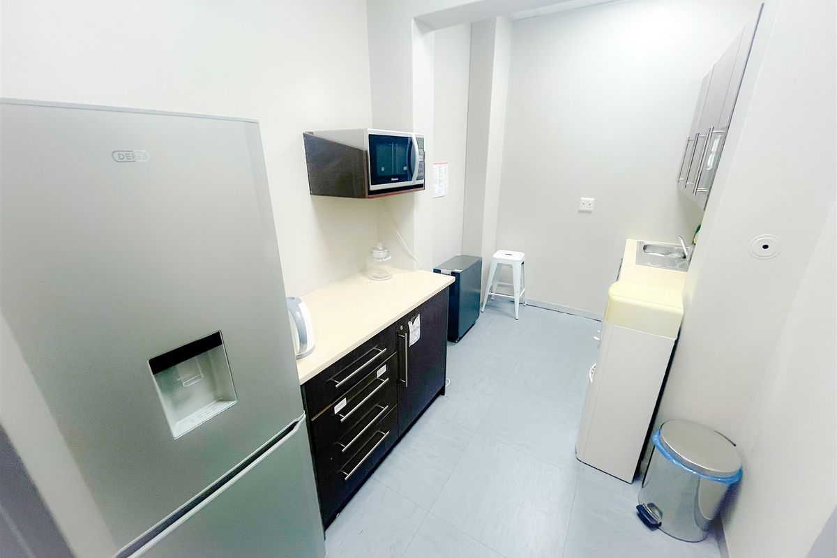 A compact office kitchenette featuring built-in cabinetry, a stainless steel sink, and a dedicated space for appliances.