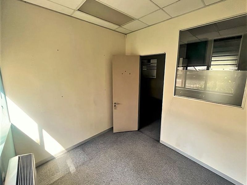An empty office space featuring carpet flooring, a suspended ceiling, an internal window, and a wall-mounted air conditioning unit.