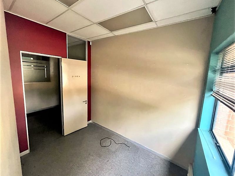 A vacant office space featuring carpet flooring, a suspended ceiling, and large windows with venetian blinds, ready for refurbishment.