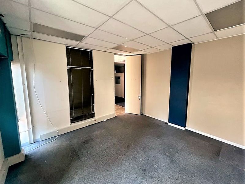 An empty office space featuring a suspended ceiling, carpeted flooring, and vertical window blinds, ready for customization.