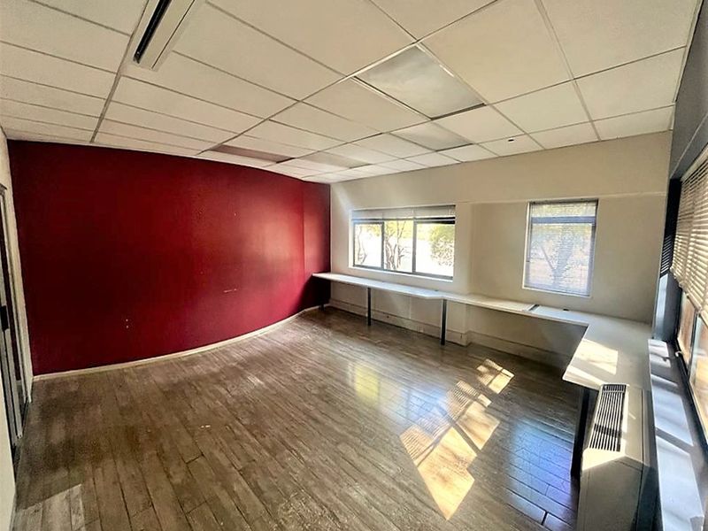 An empty office space featuring a suspended ceiling, built-in desk surfaces, and an HVAC unit, with large windows providing natural light.