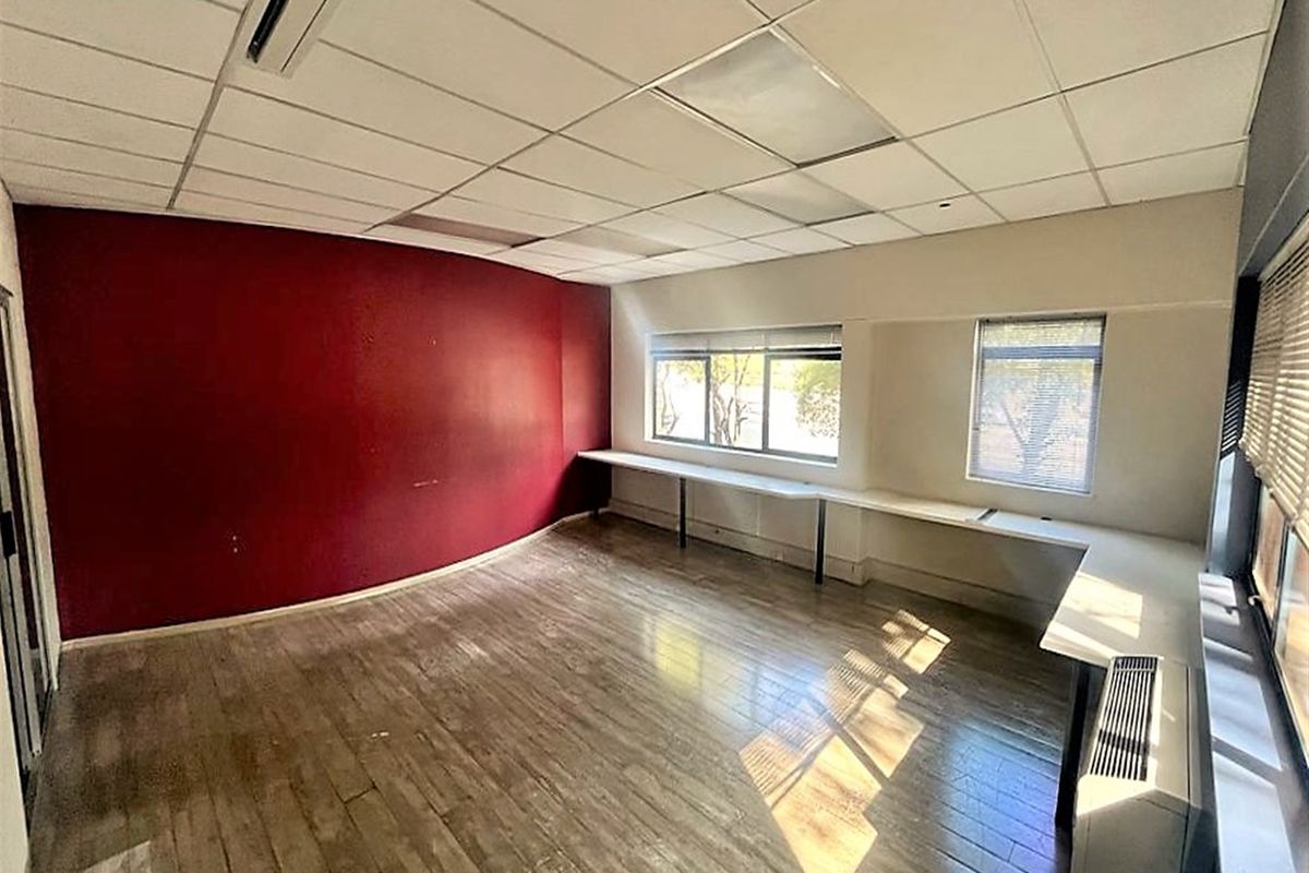 An empty office space featuring a suspended ceiling, built-in desk surfaces, and an HVAC unit, with large windows providing natural light.