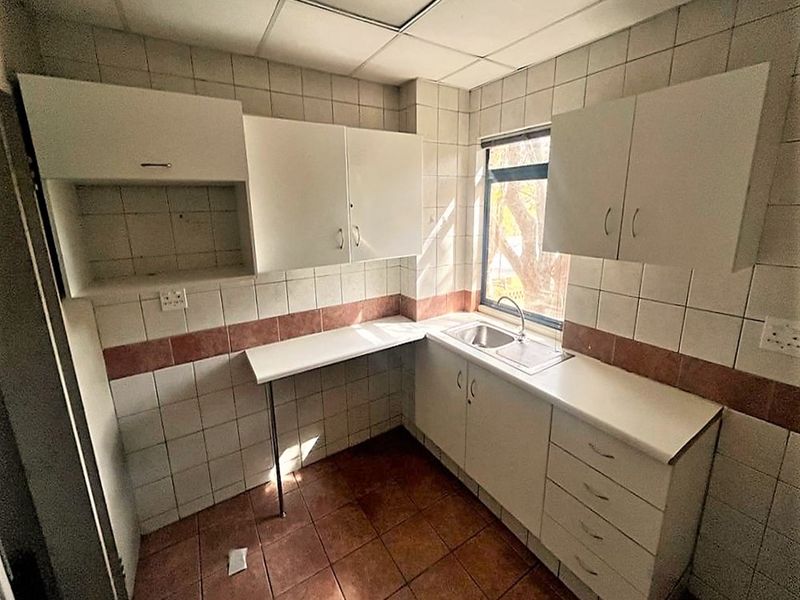 A compact, empty kitchenette featuring built-in white cabinetry, tiled surfaces, and a stainless steel sink, suitable for office staff use.