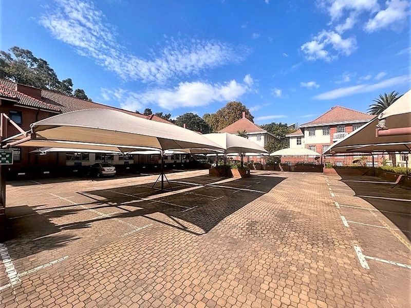 A well-maintained paved parking area featuring multiple shade cloth carports, providing ample covered parking space for the office property.