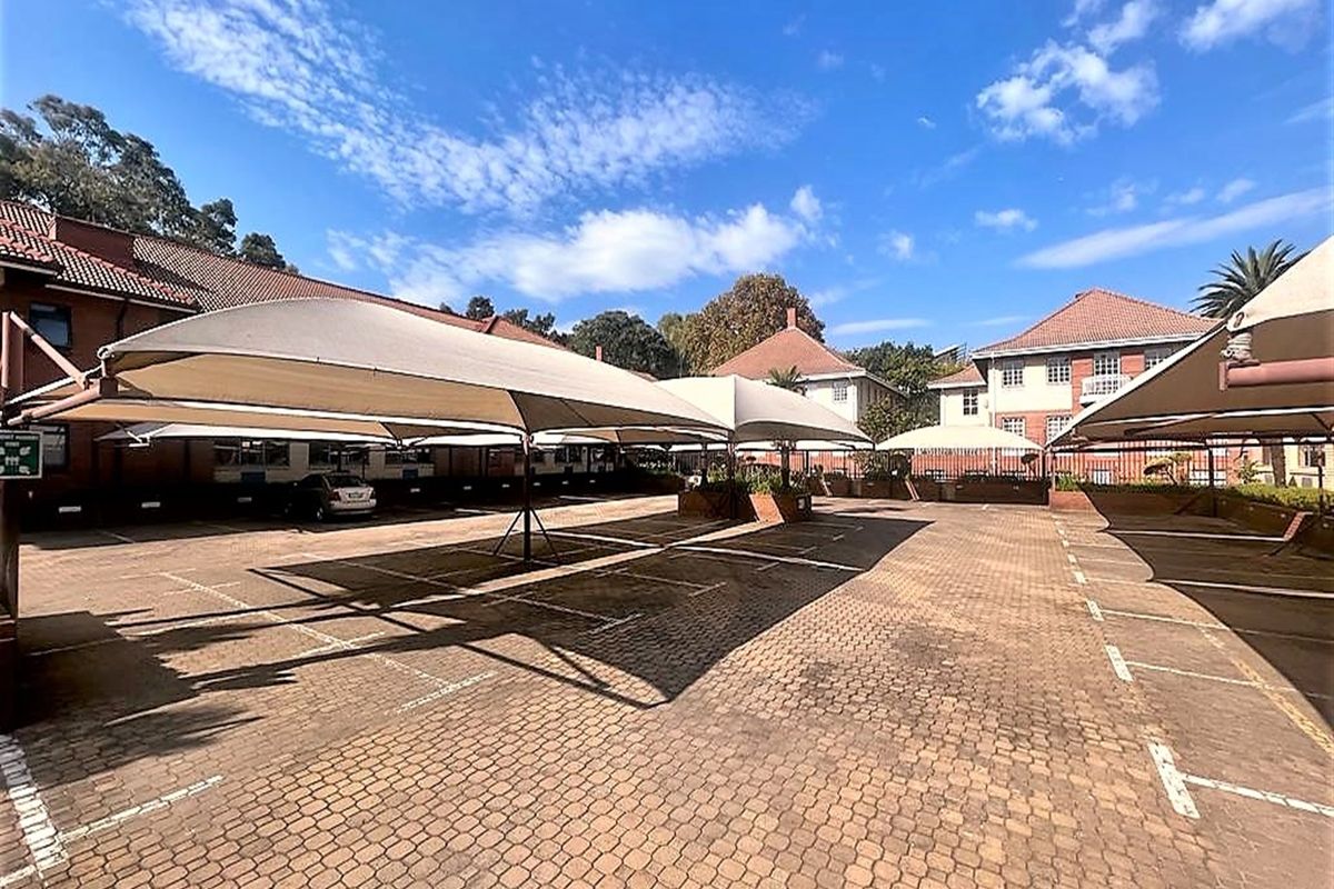 A well-maintained paved parking area featuring multiple shade cloth carports, providing ample covered parking space for the office property.