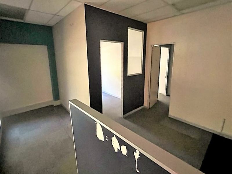 Empty office space featuring a suspended ceiling, partition walls with internal windows, and carpeted flooring, requiring cosmetic updates.