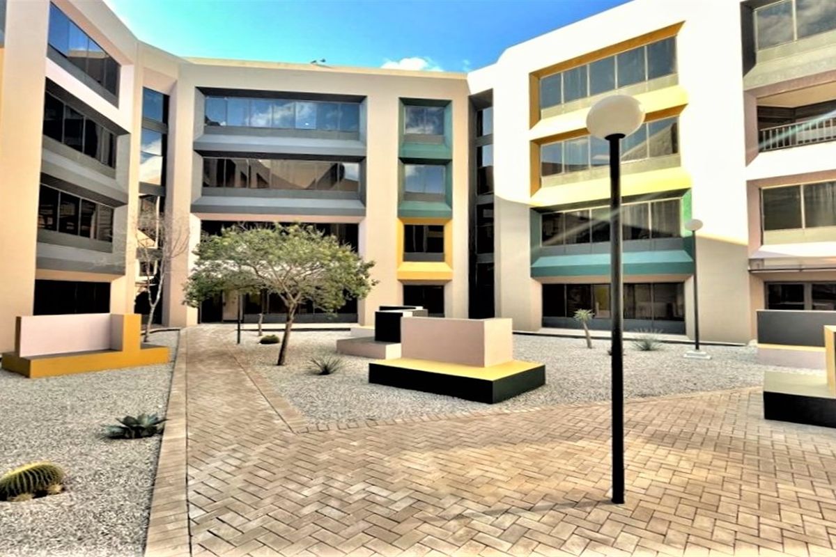 A modern office building courtyard featuring paved walkways, gravel landscaping, and integrated seating structures surrounded by multi-story office facades.
