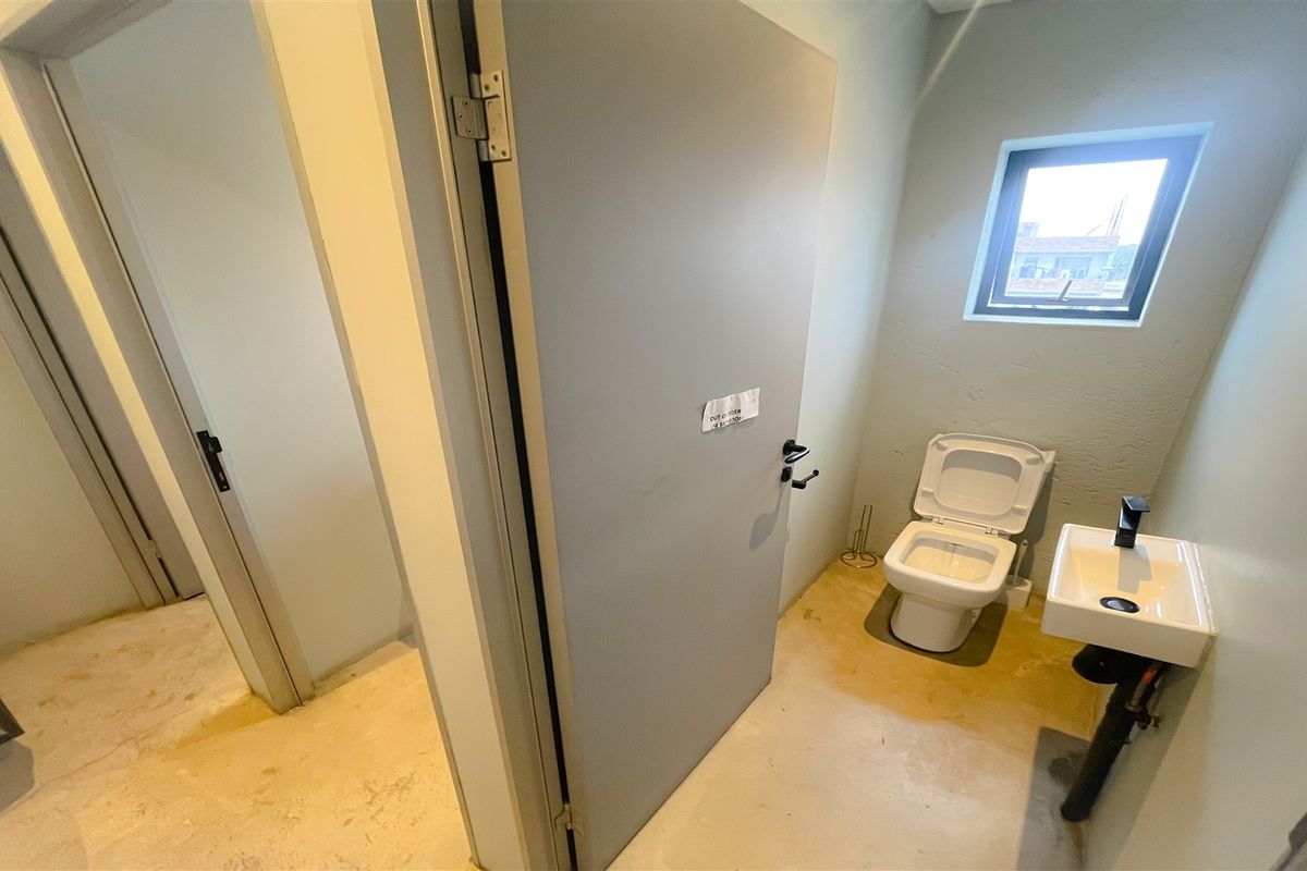 A functional office restroom featuring a wall-mounted basin, a standard toilet, and neutral wall finishes.
