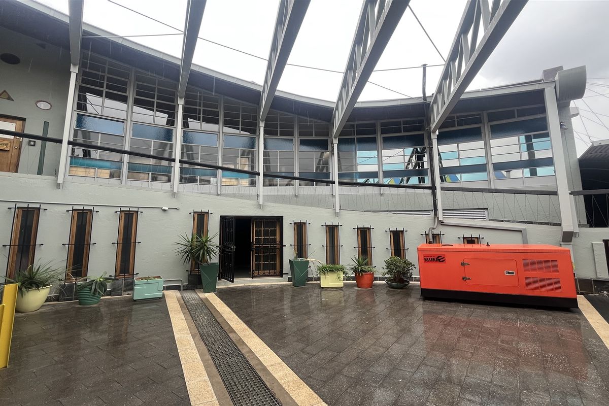 A paved courtyard area featuring a modern steel-framed roof structure, large glass windows, and a dedicated exterior power generator unit.