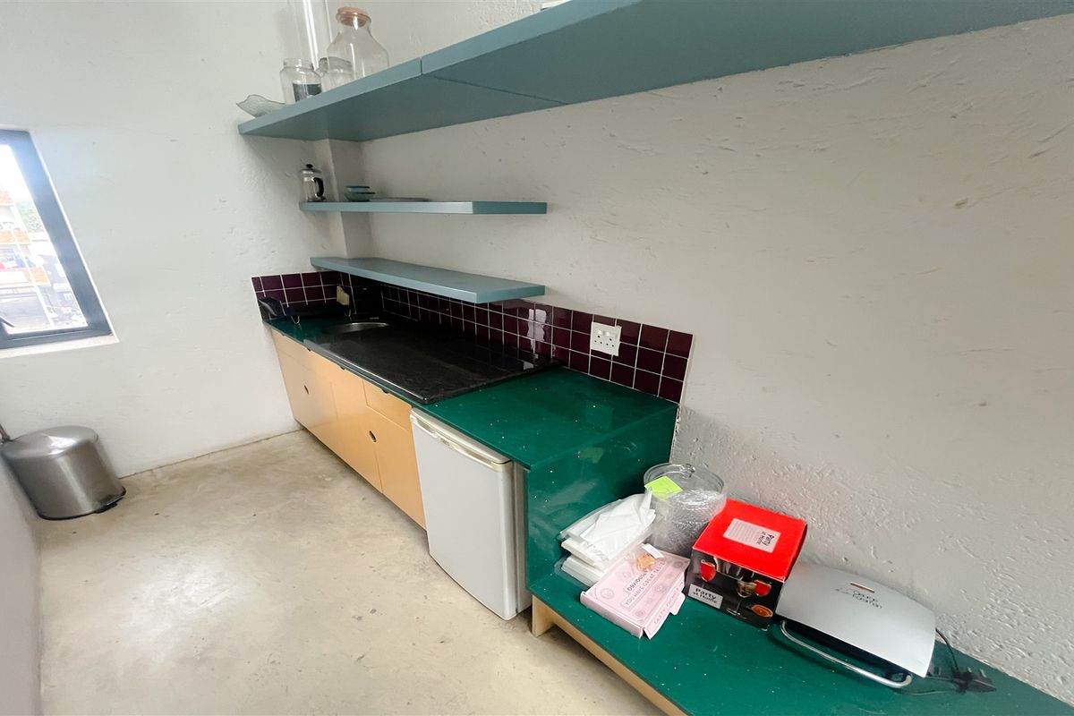 A compact office kitchenette featuring built-in cabinetry, a sink, and open shelving with a tiled backsplash.