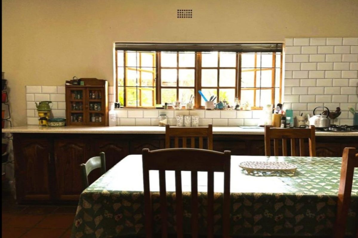 A rustic kitchen featuring wooden cabinetry, a white subway tile backsplash, and classic terracotta flooring, illuminated by natural light from timber-framed windows.