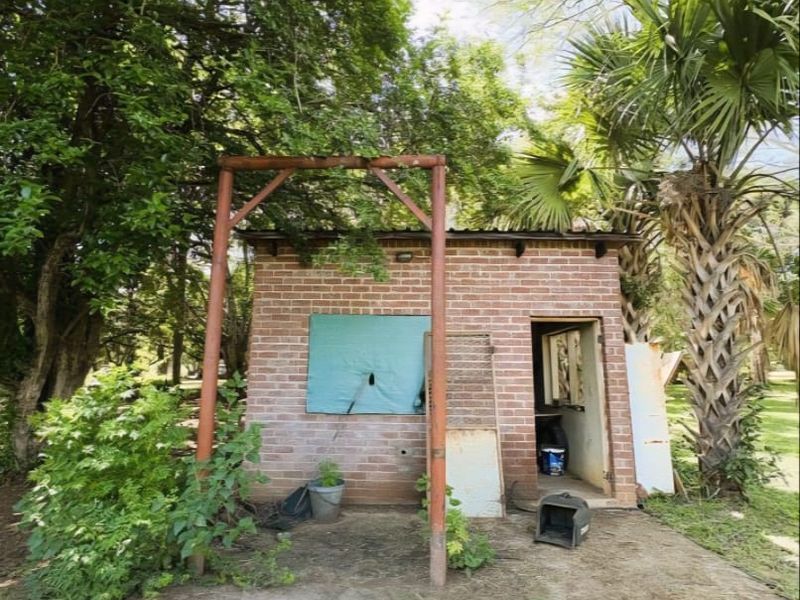 A small brick utility outbuilding on the farm property featuring a metal frame structure and concrete base, requiring maintenance and exterior restoration.