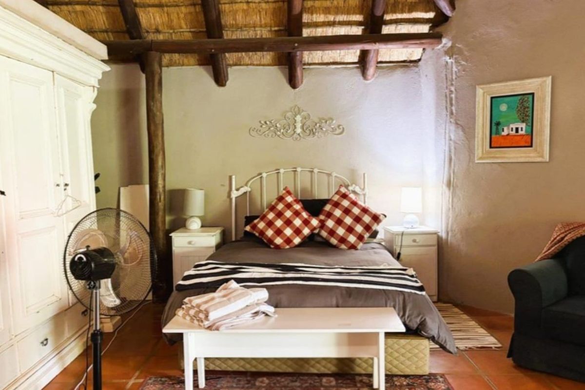 A rustic bedroom featuring a traditional thatched roof with exposed timber rafters, textured walls, and terracotta floor tiles.