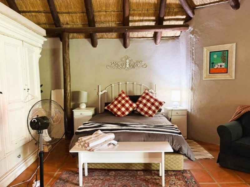 A rustic bedroom featuring a traditional thatched roof with exposed timber rafters, textured walls, and terracotta floor tiles.