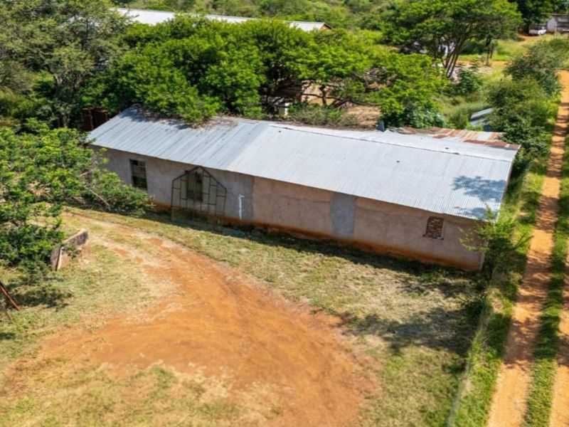 Aerial view of a rural farm building featuring a corrugated metal roof, situated on a large plot with a dirt driveway and surrounding vegetation.