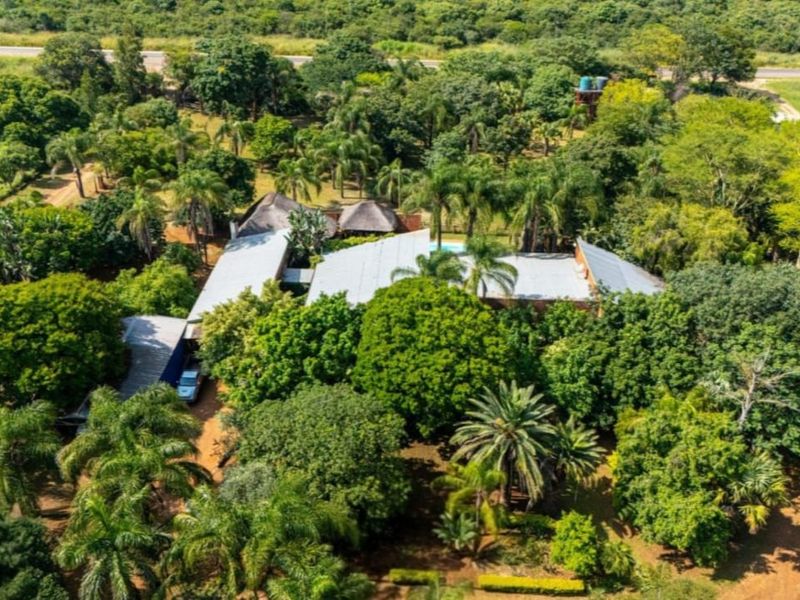 Aerial view of a farm property featuring multiple roof structures, a swimming pool, and extensive mature landscaping set within a lush, green environment.