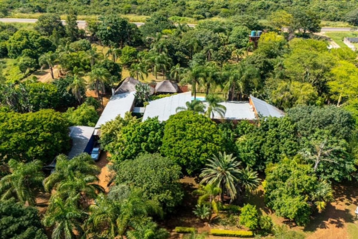 Aerial view of a farm property featuring multiple roof structures, a swimming pool, and extensive mature landscaping set within a lush, green environment.