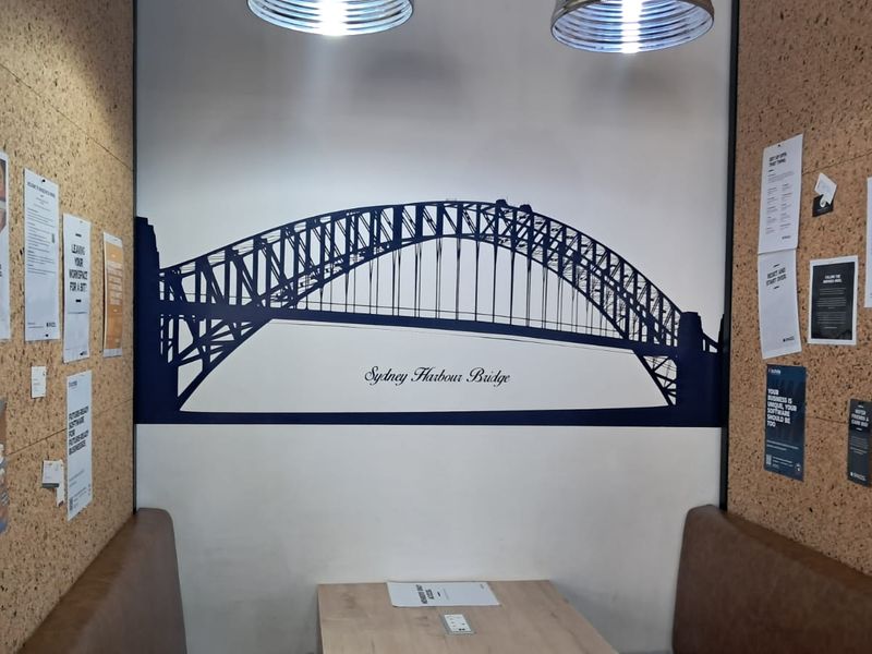 A modern office booth featuring cork wall paneling, built-in bench seating, and a Sydney Harbour Bridge wall graphic.