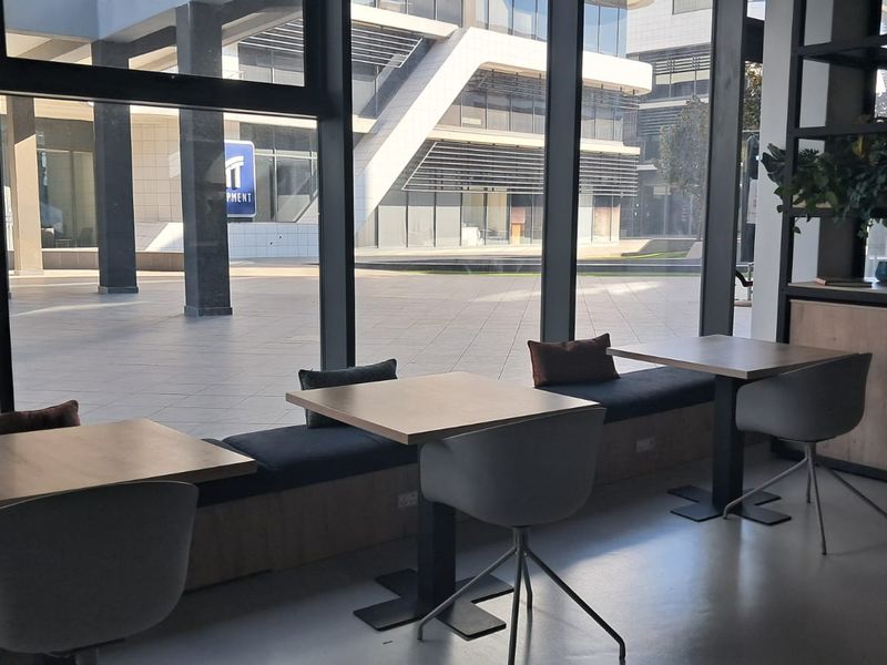 Modern office space featuring floor-to-ceiling windows, built-in bench seating, and polished concrete floors with views of the surrounding business complex.