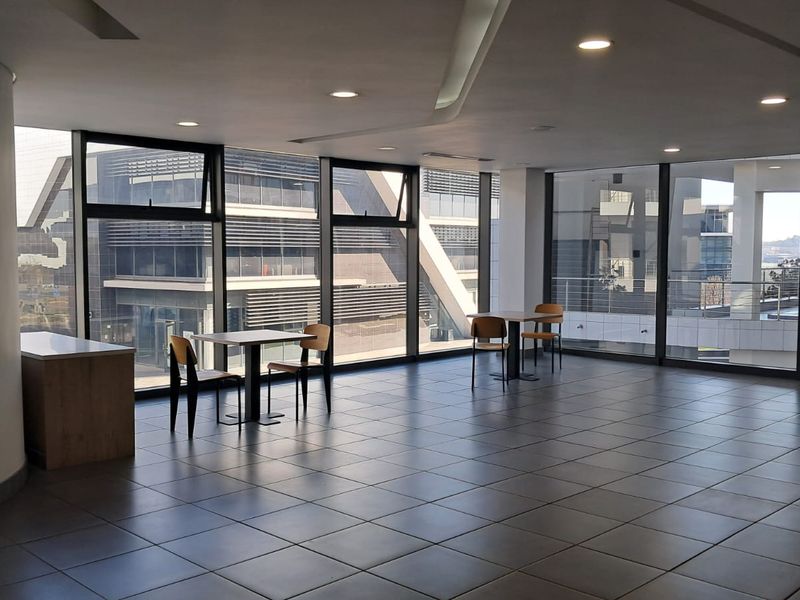 Spacious modern office area featuring extensive floor-to-ceiling windows, tiled flooring, and recessed lighting, offering a bright and professional workspace environment.