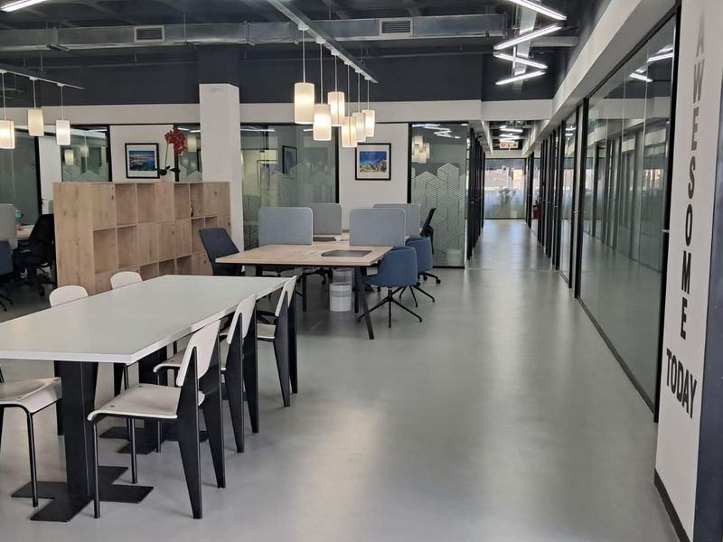 Modern open-plan office space featuring polished concrete floors, glass partition walls, exposed industrial ceilings, and integrated storage cabinetry.