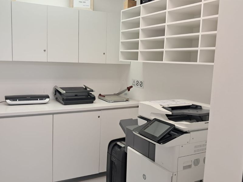 A functional office utility and storage area featuring extensive built-in cabinetry, open shelving, and a clean laminate workspace.