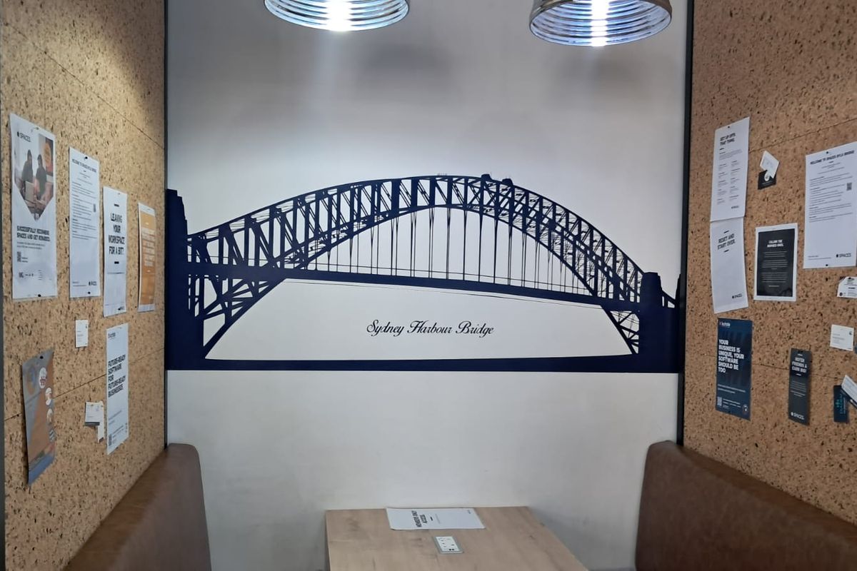 A modern office booth featuring cork wall paneling, built-in bench seating, and a Sydney Harbour Bridge wall graphic.