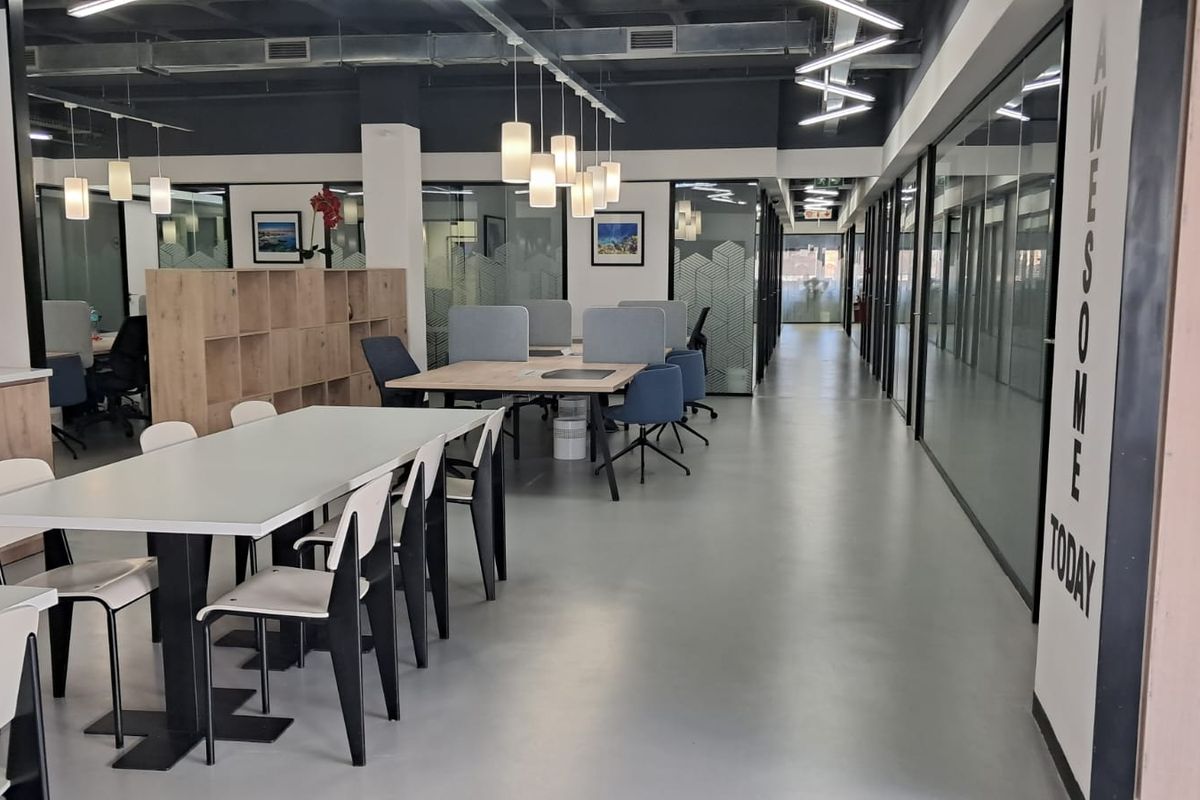 Modern open-plan office space featuring polished concrete floors, glass partition walls, exposed industrial ceilings, and integrated storage cabinetry.
