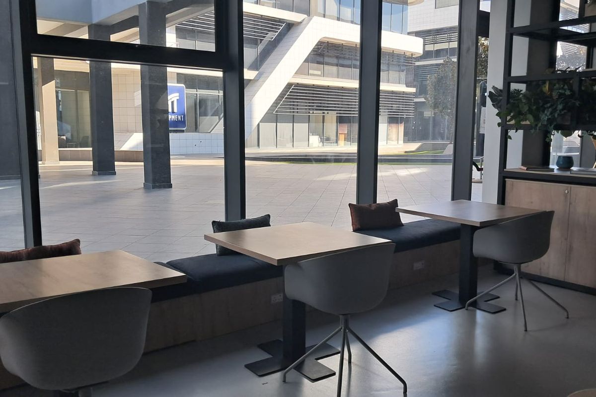 Modern office space featuring floor-to-ceiling windows, built-in bench seating, and polished concrete floors with views of the surrounding business complex.